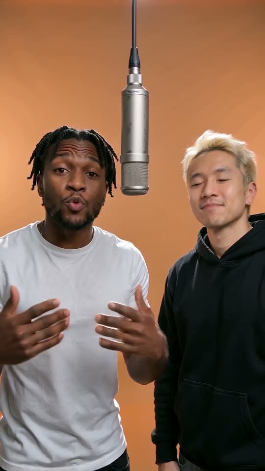 Two friends rapping at one silver microphone hanging in an orange booth, a 9:16 frame from an AI Rap Video render
